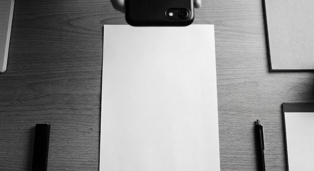 A phone held above a sheet of paper on a desk, photographing it