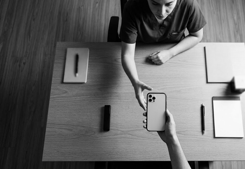A phone held out across a desk to a clinician, who is reaching for it